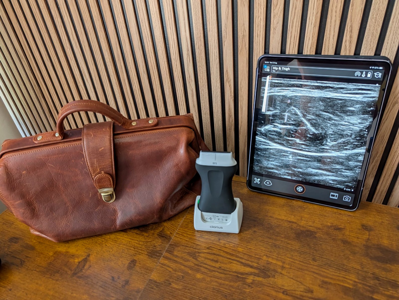 Doctor's leather bag beside a wireless ultrasound probe and a tablet showing a muscle scan